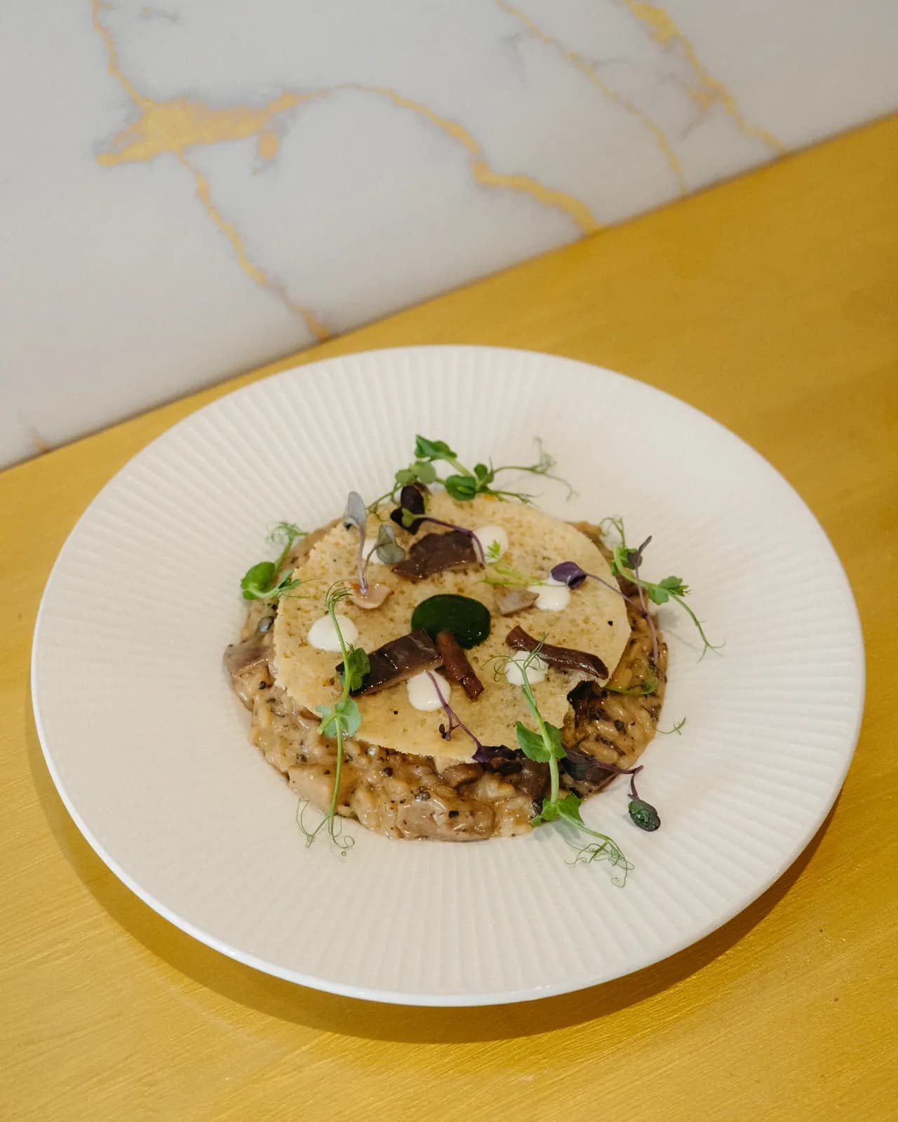 Risotto Acquerello con setas y velo de parmesano, servido en mesa de mármol