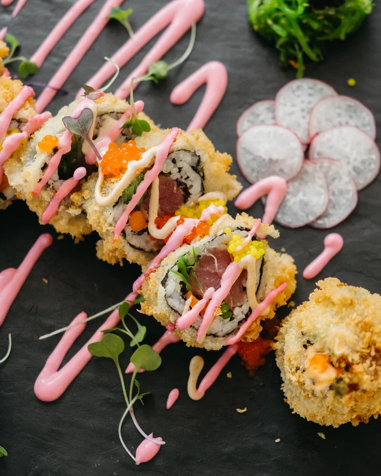 Rolls de sushi rebozados en tempura con salsa rosa, atún y tobiko sobre pizarra negra