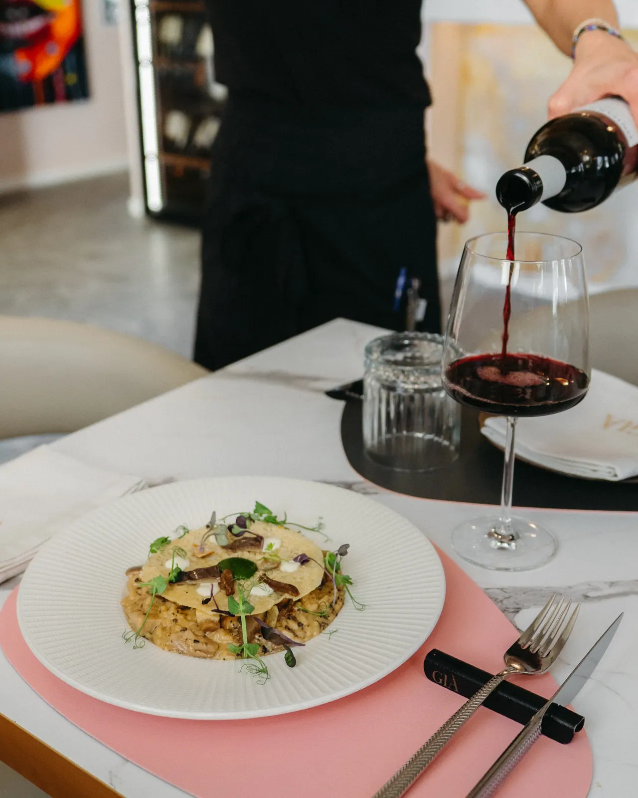 Pasta scialatielli servida con vino tinto siendo descorchado · mantel rosa palo y mármol